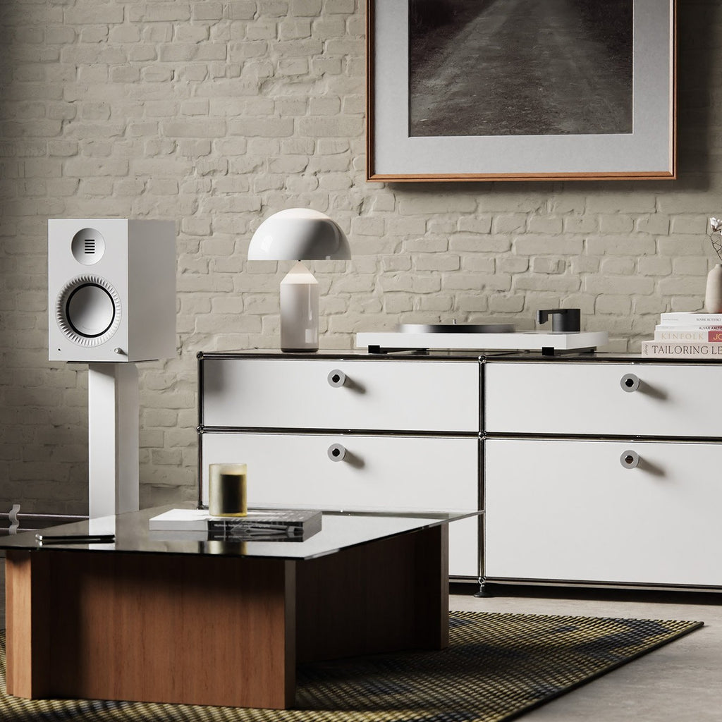 Kanto Audio TUK Grand in Matte White on stands beside a sideboard against a brick wall