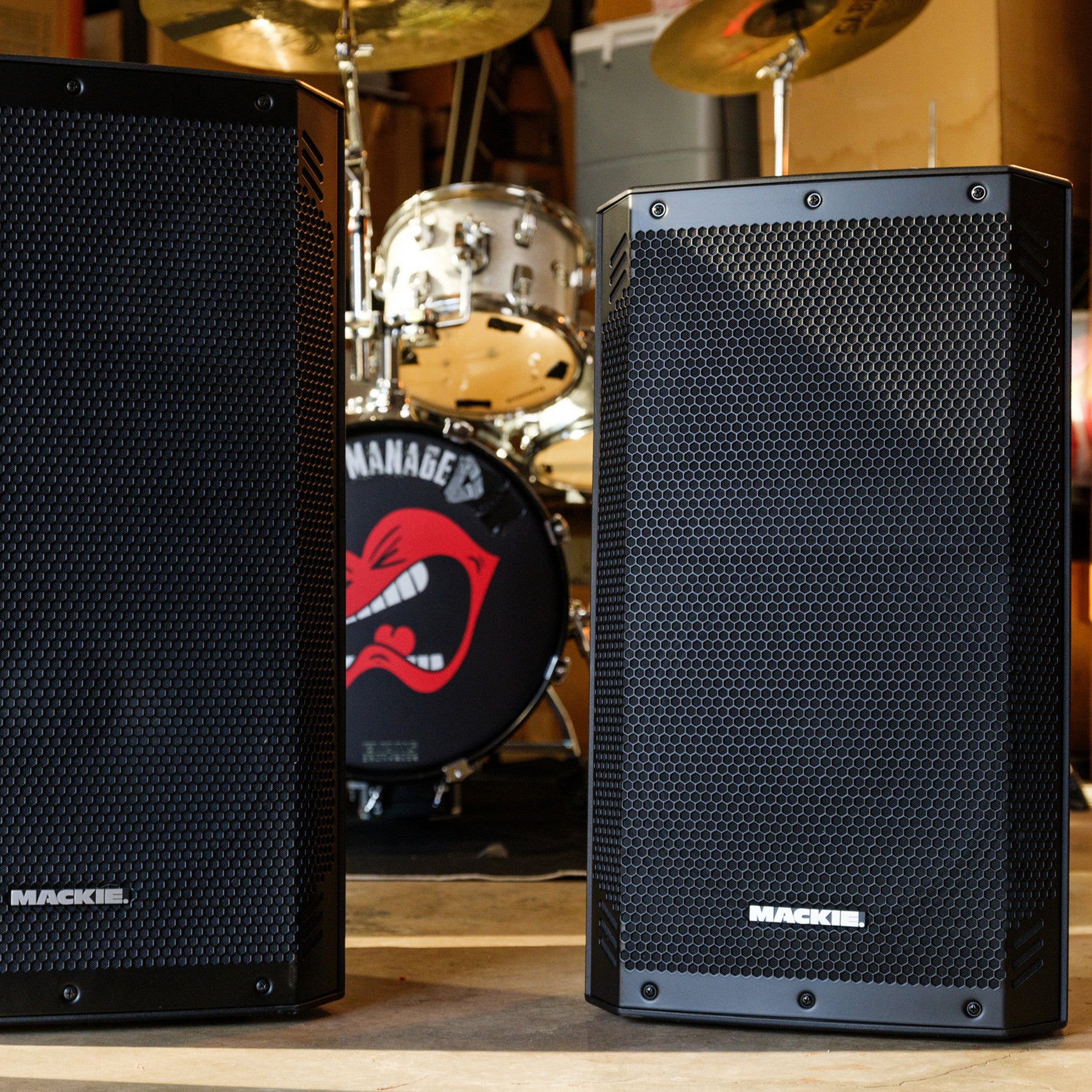 Mackie Thrash15v2 and Thrash12v2 powered PA speakers set up in a rehearsal room next to a drum kit